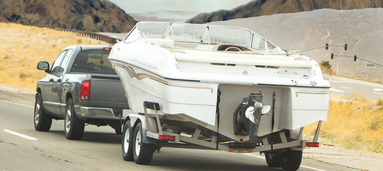 A truck towing a boat securely on a trailer, cruising down a sunny road in the summer, illustrating summer boating safety tips