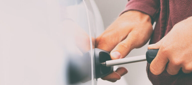 A person wearing a hoodie crouching beside a car with a screwdriver in hand, suggesting potential car theft. The image is accompanied by the text 'Preventative Auto Theft Tactics